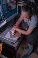 Young white-skinned Latina woman doing printing work using the screen printing and printing with meshes method. It could be for industry or sales. Advertising uses different tools or objects. She is h