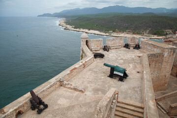 Historical bronze cannons and a turret at the fortified walls of Castillo del Morro or San Pedro de la Roca fortress XVII century fortress, and the entrance of Santiago de Cuba bay.