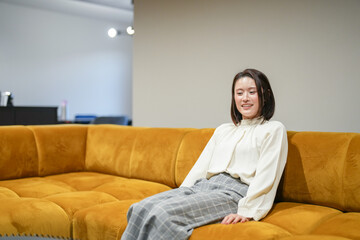 A Japanese woman in her 30s is relaxing on the sofa in her living room.