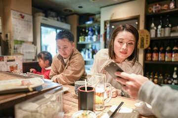 A Japanese parent and child, a woman in her 30s, a 6-year-old girl, and a man in his 20s, are enjoying yakitori at an izakaya.