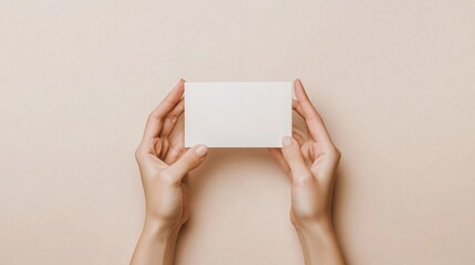 Woman's hands hold blank white card on beige background.