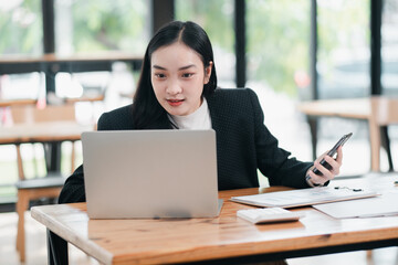 Fototapeta premium Confident businesswoman multitasking with a laptop and phone in a stylish cafe setting, showcasing remote work and modern technology.