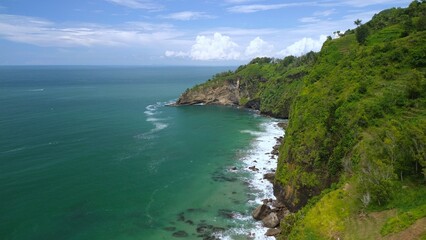 Aerial drone view of coastline with hills and trees, as well as view of coral cliffs and sea with waves from the ocean in Menganti Beach Kebumen Central Java Indonesia