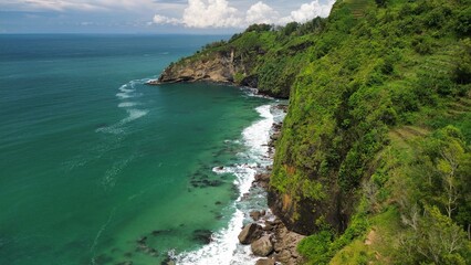 Obraz premium Aerial drone view of coastline with hills and trees, as well as view of coral cliffs and sea with waves from the ocean in Menganti Beach Kebumen Central Java Indonesia