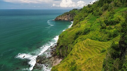 Aerial drone view of coastline with hills and trees, as well as view of coral cliffs and sea with waves from the ocean in Menganti Beach Kebumen Central Java Indonesia