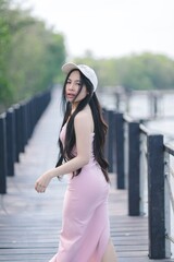 Fototapeta premium Young Woman in Pink Dress Strolling on Scenic Boardwalk by Water