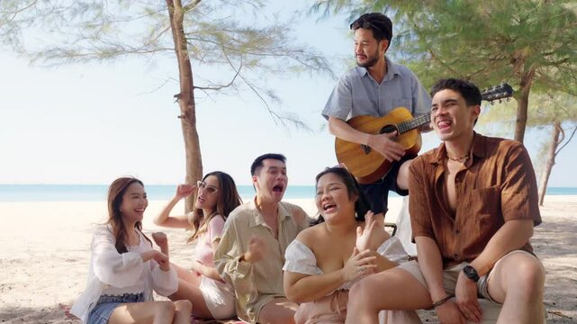 Happy man and woman travel at the sea on summer beach holiday vacation. Group of Asian people friends enjoy and fun outdoor lifestyle relaxing and picnic together on tropical island beach in sunny day