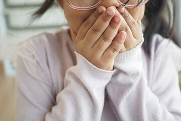 A Young Child is Covering Their Face with Hands in a Cozy Indoor Setting