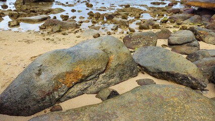 A rocky coastal landscape with scattered boulders in Hon Chong cape rocks garden on the Nha Trang beach, Vietnam with a calm sea and mountains in background.