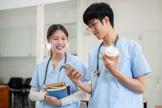 Two happy Asian medical students in scrubs are standing in their classroom and discussing.
