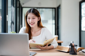 Fototapeta premium A beautiful Asian female college student working remotely from a cafe or studying in a library.