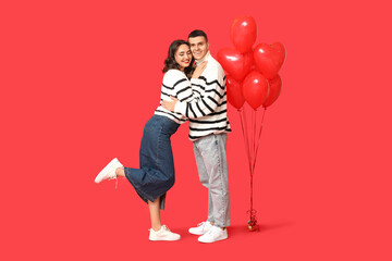 Loving young couple with heart-shaped balloons on red background. Celebration of Saint Valentine's Day