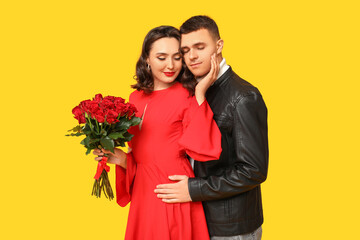 Loving young couple with bouquet of beautiful roses on yellow background. Celebration of Saint Valentine's Day