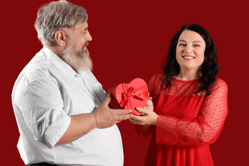 Beautiful mature couple with heart-shaped balloons and gift box on red background. Valentine's Day celebration