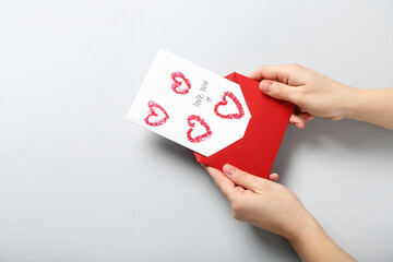 Female hands with red envelope and greeting card on grey background, closeup. Valentine's Day celebration