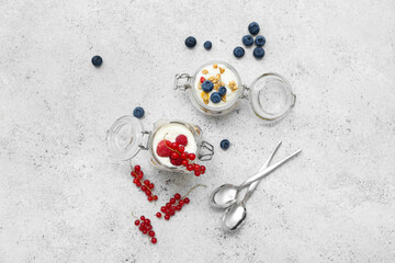 Jars of tasty granola with yogurt on light grunge background