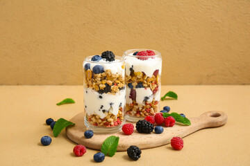 Wooden cutting board and glasses of tasty granola with yogurt on beige background