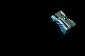 A close-up of a metal pencil sharpener against a dark, black background, showcasing its sleek and...