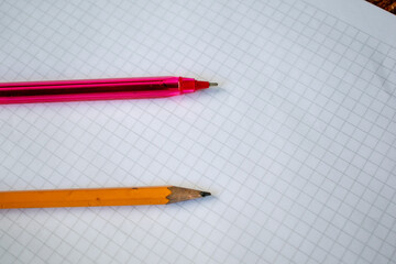 A pencil and red pen placed on a white grid paper sheet, symbolizing creativity, writing, and organization. This simple and versatile image is perfect for projects related to education, stationery