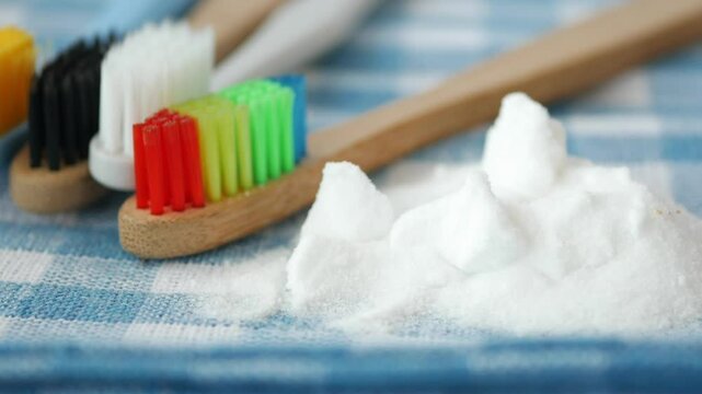 A wooden bowl of baking soda, a bamboo toothbrush, and a glass jar on a fabric