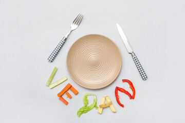 Composition with plate, cutlery and word VEGAN made of vegetables on grey background