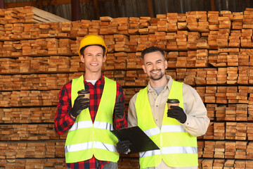 Male carpenters with coffee cups near wooden planks at sawmill