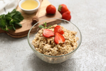 Bowl with tasty oatmeal and strawberry on grey grunge background