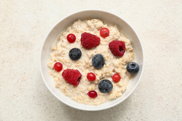 Bowl with tasty oatmeal and berries on beige grunge background