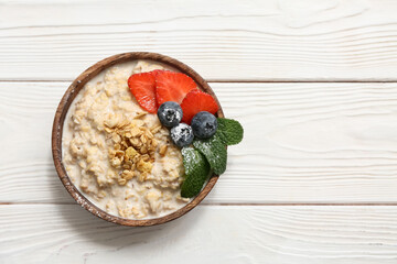 Bowl with tasty oatmeal and berries on white wooden background