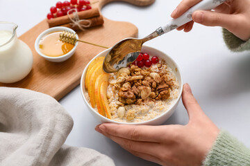 Female hands with tasty oatmeal, berries and nuts in bowl on white background