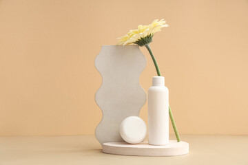 Plaster stands, flower, jar and bottle with cosmetic products on beige background
