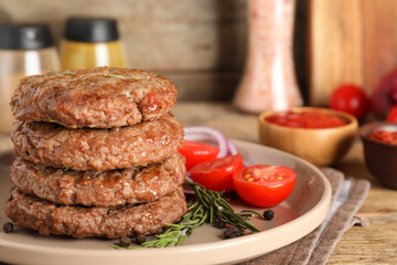 Plate with stack of tasty meat cutlets, cut tomatoes, rosemary and peppercorns on wooden background