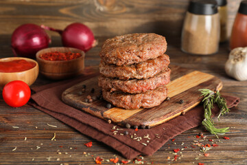 Board with stack of tasty meat cutlets, peppercorns and rosemary on wooden background