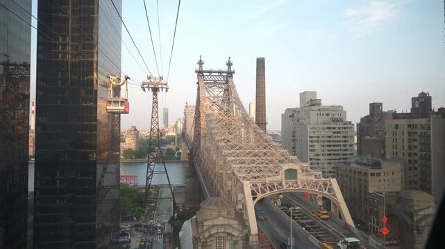 This image highlights the iconic Queensboro Bridge spanning the East River with the Roosevelt Island Tramway passing alongside. The urban skyline and river create a stunning cityscape view.