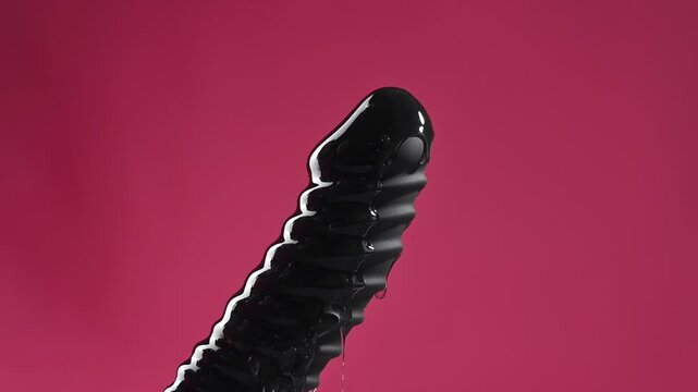 Lube pouring on black dildo on pink background. 