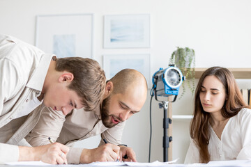 Script writing. Studio team. Girl watches as men taking notes sign document lighted room. Paper work creative media ads project.
