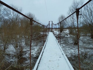 Wooden footbridge over a river on tensioned steel cables with a thin layer of white snow. Long...