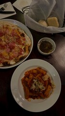 pizza with ham and cheese next to a pasta dish