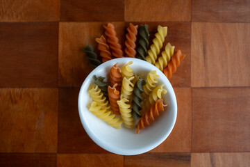 Pasta fusilli cruda acomodada ordenadamente saliendo de plato pequeño blanco centrada