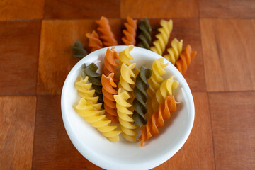 Pasta de tornillo cruda acomodada sobre plato pequeño redondo sobre base de madera con pasta afuera