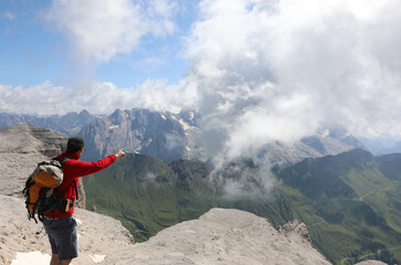 backpacking hiker pointing toward the summit of Mount Marmolada in summer in northern Italy on the European Alps