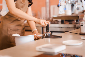 An Asian woman, a skilled female barista,makes coffee while opening her coffee shop.carefully prepares the perfect brew,providing excellent coffee preparation service in a welcoming cafe environment