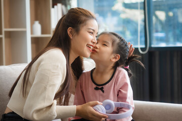 Asian young mother and her daughter sit together on the sofa in the cozy living room, working on homework at the desk, creating a warm and supportive atmosphere for learning, love, hug, mother days.