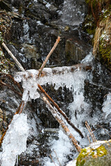 Stunning winter scene showcasing a frozen waterfall flowing over mossy rocks, with icicles hanging from a wooden log, creating a picturesque natural ice formation