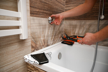 Professional plumber working carefully, installing or repairing bathtub faucet in modern bathroom