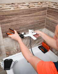 Professional plumber working on installing or repairing faucet in modern bathroom using adjustable...