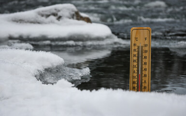 Wooden thermometer showing sub zero temperature inserted in frozen river covered with snow and ice...