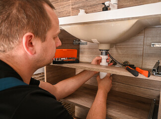 Professional plumber working under sink, fixing pipes and installing new plumbing fixture in modern bathroom