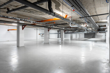 Empty industrial space featuring concrete flooring and exposed piping in a well-lit underground area