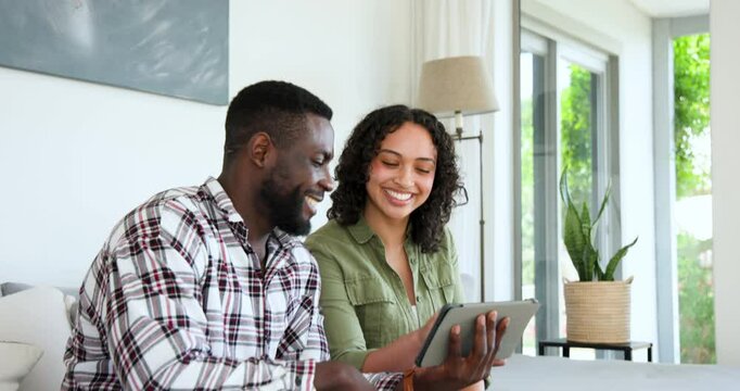 Smiling multiracial couple using tablet at home, enjoying relaxed conversation together